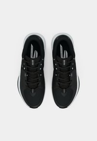 Baskets de sport noires avec un dessus texturé, semelle extérieure blanche et accents contrastants. Comprend un design à lacets et une marque sur la languette.