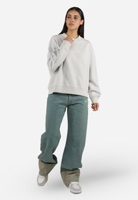 Light grey sweatshirt with crew neck and ribbed cuffs, paired with loose-fit green denim jeans and white sneakers.