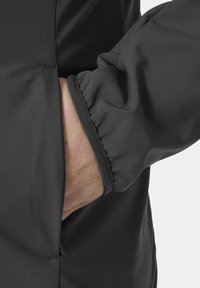 Mano de una persona insertada en el bolsillo lateral de una chaqueta negra con puño elástico en la manga.