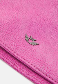 Portafoglio sintetico rosa con superficie testurizzata, dotato di un piccolo emblema metallico a forma di ali. Cuciture ai bordi e design minimalista.
