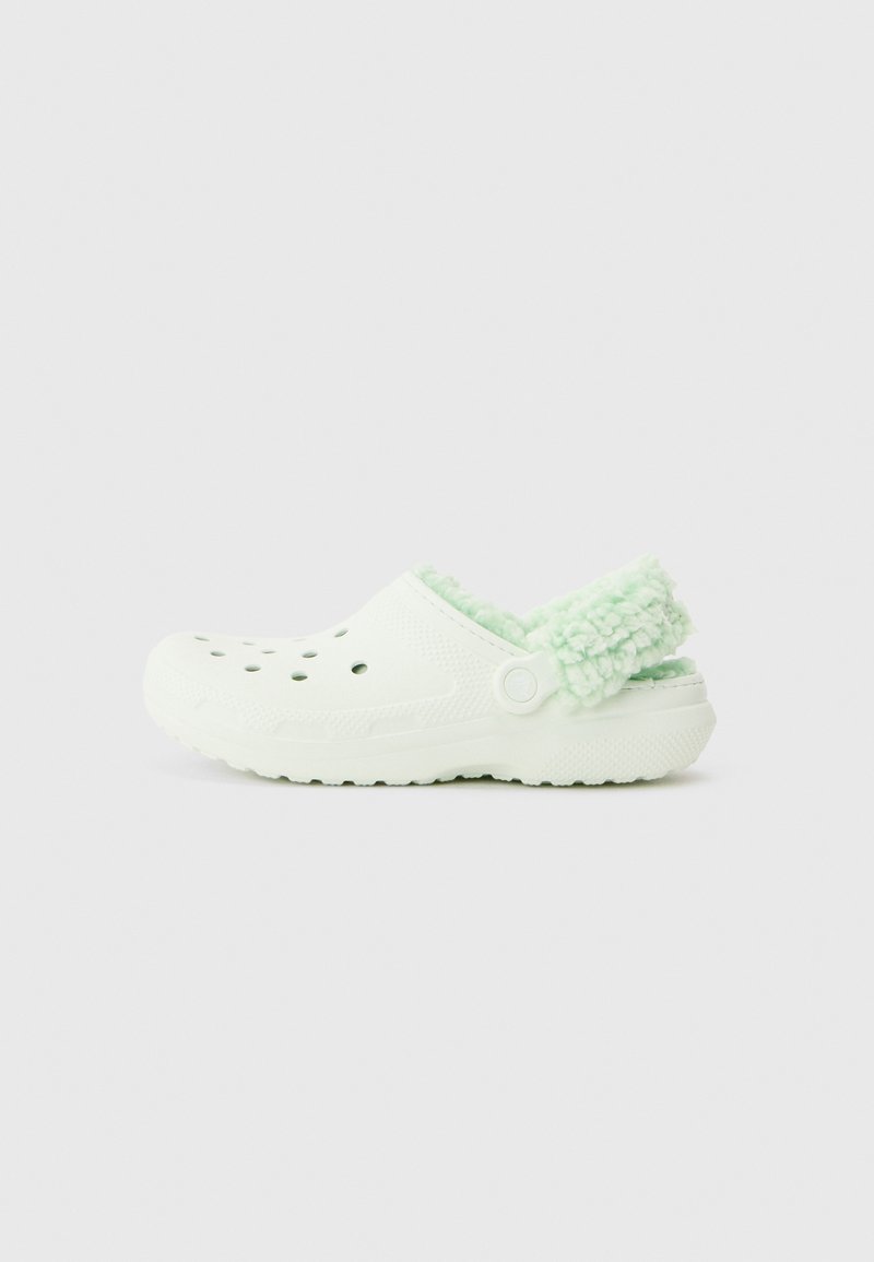 Weiße Clogs ohne Schnürung mit Belüftungsöffnungen und einem hellgrünen, flauschigen Futter am Fersenriemen, vor einem einfarbigen Hintergrund präsentiert.