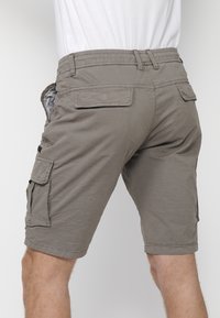 Khaki krāsu cargo šorti ar elastīgu jostasvietu, vairākiem sānu kabatām un nokasītu tekstūru. Šuvju apdare gar šuvēm.