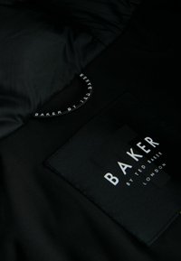 Črn notranji material ima teksturirano oznako z napisom "BAKER BY TED BAKER" v belem tisku, ki prikazuje eleganten, sodoben dizajn.