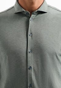 Lichtgroene polo met een zachte textuur, puntige kraag en zes knopen; het heeft subtiele heathering in de stof.