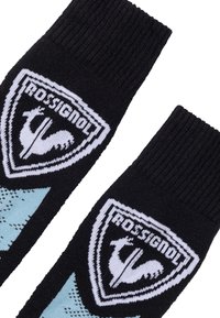 Sorte strikkede sokker med ribbede manchetter, der har hvide og blå skjoldlogoer med en høne og "Rossiignol" tekst på forsiden.