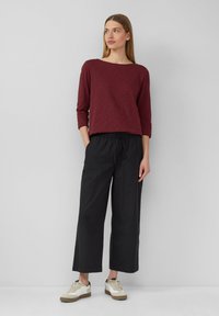 Weinrot langärmliges Oberteil kombiniert mit schwarzen weiten Hosen und weißen Sneakers. Der Stoff scheint weich mit einem lässigen Schnitt und elastischem Bund zu sein.