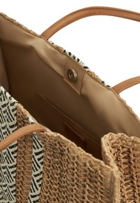Woven tote torba od slame s tušim kožnim ručkama, s crno-bijelim geometrijskim uzorkom unutrašnjosti i zaklopcem na pritisk.
