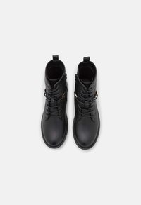 Botines negros de tobillo hechos de piel sintética texturizada, con un diseño de cordones y una cremallera lateral con acentos metálicos.