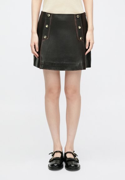 Mini-jupe en cuir noir avec des accents de boutons dorés sur les poches avant et des coutures contrastantes. Texture lisse, forme évasée.