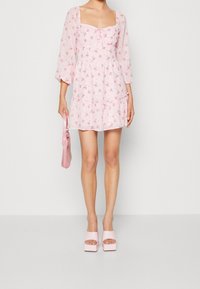 Vestido floral rosa con escote cuadrado, mangas largas transparentes, falda en capas y un detalle de lazo. Combinado con zapatos de plataforma rosa y un bolso a juego.