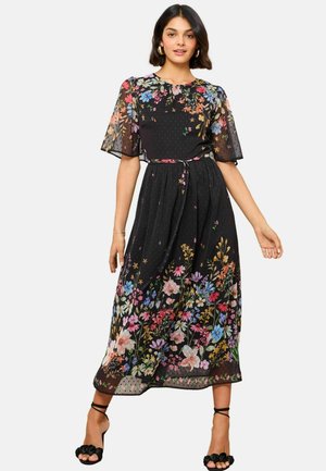 Black floral maxi dress with short, sheer sleeves, featuring a mix of colorful flowers and a cinched waist with a fabric tie.