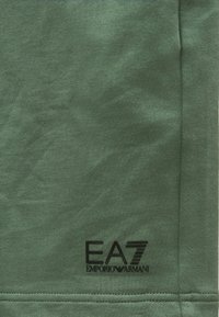 Roheline puuvillane kangas, sileda tekstuuriga; alumises osas on must EA7 Emporio Armani logo. Lihtne disain, muster puudub.