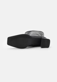 Bota negra de tacón alto con punta cuadrada y textura suave, con suela de goma y tacón grueso para mayor estabilidad.
