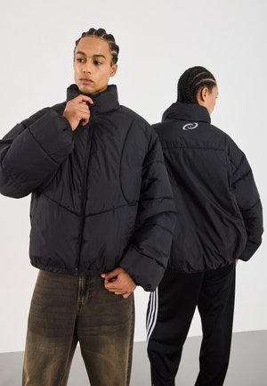Črno puffer jakno z visokim ovratnikom in sprednjim zadrgo. Opremljena je s prešito zasnovo, elastičnimi manšetami in logotipom na hrbtu.