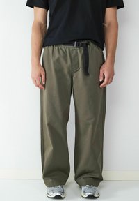 Olijfgroene, wijde broek gemaakt van lichtgewicht stof, met een elastische tailleband en een zwarte verstelbare riem.