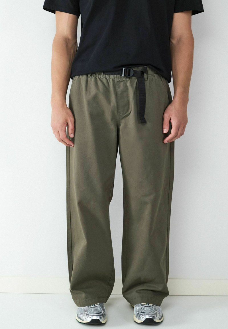 Olijfgroene, wijde broek gemaakt van lichtgewicht stof, met een elastische tailleband en een zwarte verstelbare riem.