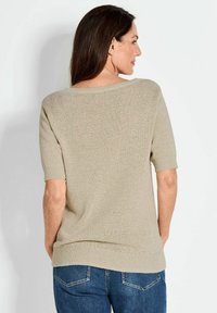 Maglione beige a maglia con scollo ampio, maniche corte e orlo a coste. Indossato con jeans blu, che mostrano un tessuto texturizzato.
