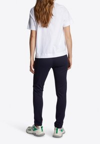 Vit bomullströja, marinblå joggers med smal passform och ljusgrå sneakers med gröna detaljer. Bakifrån syns klädkombinationen.