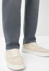 Sneaker beige con accenti in suede testurizzato e pelle, lacci bianchi e suole in gomma spessa, abbinati a jeans grigi a gamba dritta.