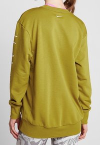 Sweat-shirt vert olive avec une coupe ample, des poignets et un ourlet côtelés. Présente un petit logo blanc au niveau de la nuque à l'arrière et une texture unie.