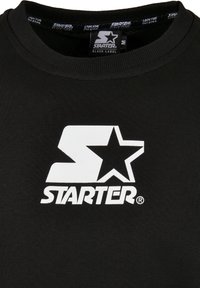 T-shirt noir à col rond avec logo blanc « Starter » présentant un « S » stylisé et une étoile centrés sur la poitrine.