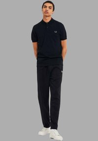 Polo nero a maniche corte con colletto, dotato di un piccolo logo ricamato. Abbinato a pantaloni neri e sneakers bianche.