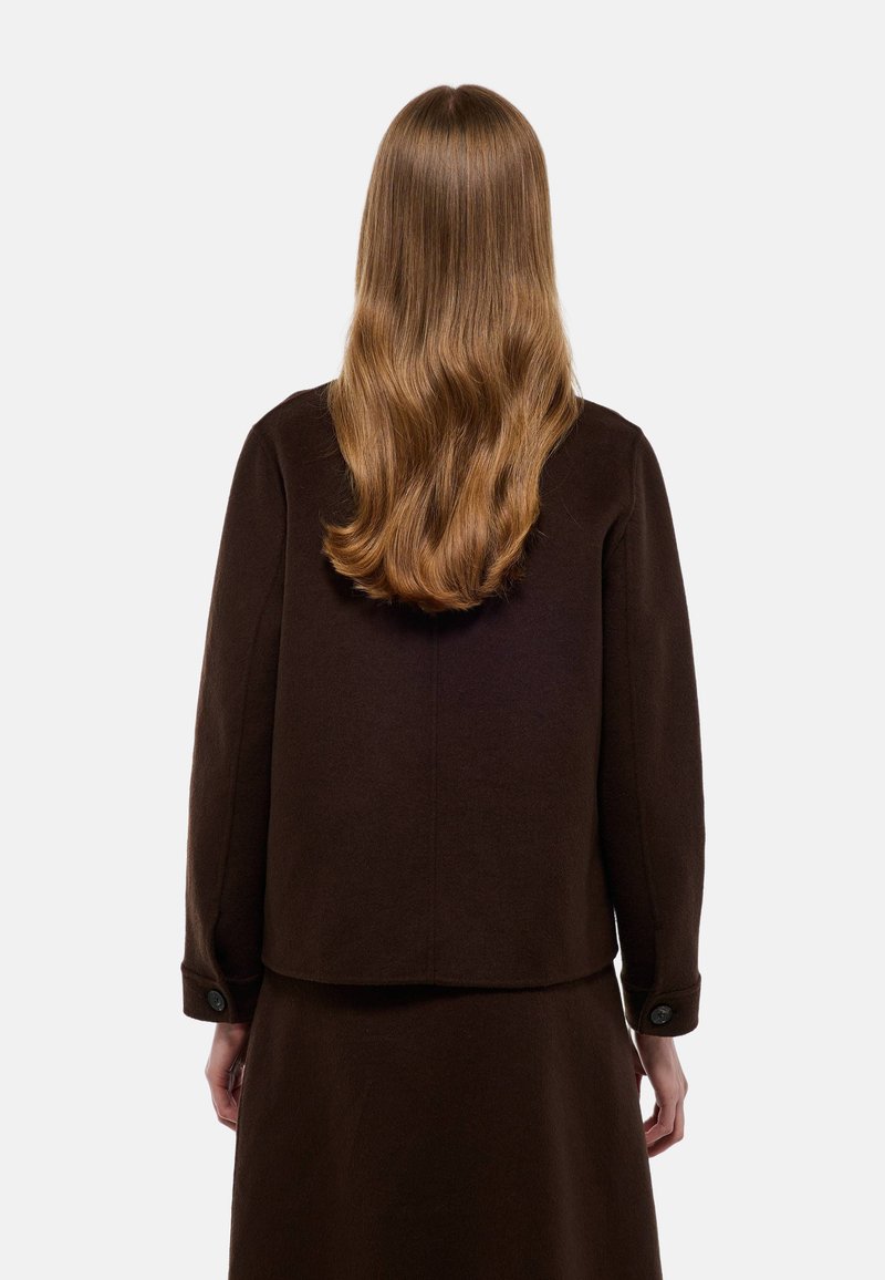 Veste en laine marron au coupe boxy, avec des poignets boutonnés et une silhouette épurée. Vue de dos, montrant une texture lisse et un design simple.