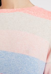 Lähikuva pehmeästä neulotusta villapaidasta, jossa on leveitä vaaleanpunaisia, beigejä, vaaleanpunaisia ja vaaleansinisiä vaakasuoria raitoja.