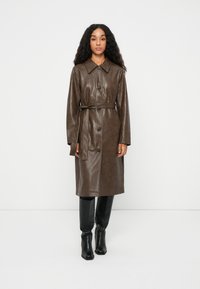 Brun læder trenchcoat med krave, frontknaplukning og bånd i taljen. Glat tekstur og mellemlang design.