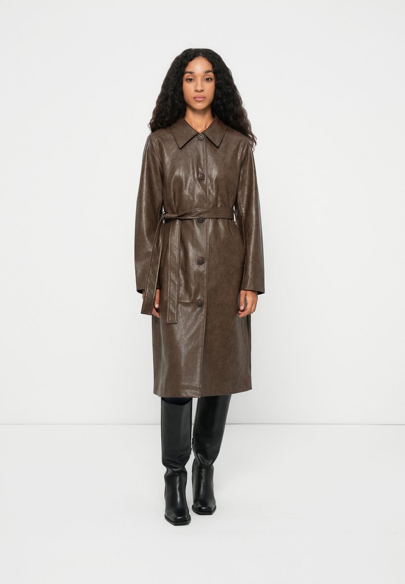 Brun læder trenchcoat med krave, frontknaplukning og bånd i taljen. Glat tekstur og mellemlang design.