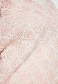 Pulover tricotat în roz moale, cu un model de diamant alb și o strălucire metalică subtilă. Textura este ușoară și intricate.