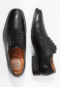 Chaussures habillées en cuir noir avec une finition lisse, un design à lacets, une semelle intérieure rembourrée et un petit talon en caoutchouc texturé.