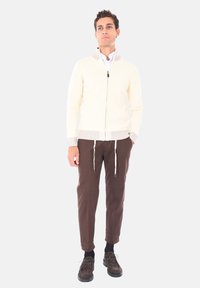 Pullover crema con zip, in maglia testurizzata e colletto a righe, abbinato a pantaloni marroni a sigaretta e calzature scure.