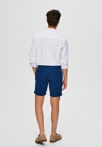 Vit långärmad skjorta med marinblå upprullade shorts. Shortsen har två bakfickor och en smidig, mjuk textur.