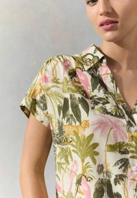 Korte mouw knoopshirt met een botanische print van roze flamingo's, groene bladeren en een tijger op een crèmekleurige achtergrond.