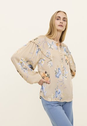 Blumenbluse in Beige mit blauem und orangefarbenem Muster, mit Rüschendetails und einer Knopfleiste, ergänzt durch lockere Ärmel.