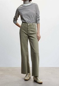 Groene wijde spijkerbroek met een hoge taille en rafelige onderranden. Gecombineerd met een zwart-wit gestreepte lange mouwtop. Beigekleurige sneakers maken de look compleet.