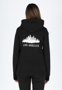Black hoodie with a front pocket, featuring a white skyline design and the text "LOS ANGELES" on the back. Soft fabric, relaxed fit.