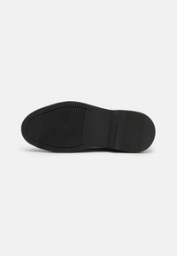 Suela de zapato negra con goma texturizada para agarre, que presenta un diseño suave y plano con patrones de tracción sutiles.
