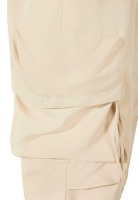 Beige cargo nadrág több zsebbel, könnyű anyagból készült, sima textúrával és varrott részletekkel a varratok mentén.