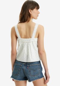 Hvid ærmeløs top med blonder og små blå mønstre, parret med slidte denim shorts, der fremviser klassisk baglomme-design.