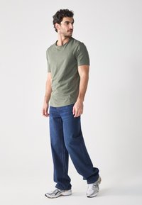 Olijfgroene t-shirt met korte mouwen, losse donkerblauwe jeans en zilveren sport sneakers. Eenvoudig ontwerp, casual uitstraling, natuurlijke stoftextuur.