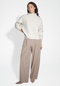 Maglione beige lavorato a maglia con colletto alto, abbinato a pantaloni palazzo marrone chiaro. Le scarpe basse in suede neutro completano l'outfit.