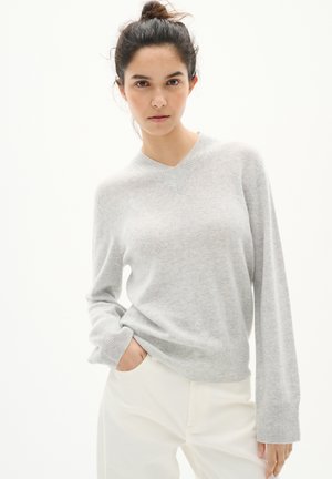Hellgrauer V-Ausschnitt-Pullover aus weichem Material, mit langen Ärmeln und gerippten Bündchen sowie lockerer Passform. Getragen mit cremefarbenen Hosen.