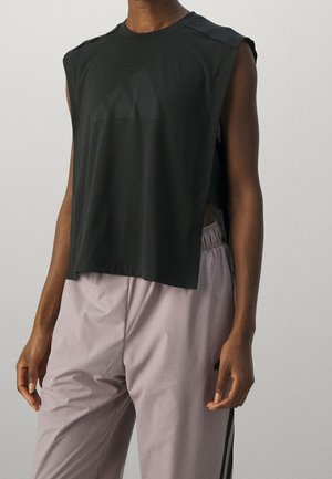 Persoon draagt een mouwloos, zwart cropped top met een subtiel Adidas-logo en losse lichtpaarse broek met zwarte zijstrepen.