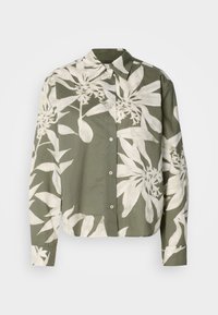 Chemise verte à boutonné avec un motif floral blanc. Fabriquée en tissu léger, avec un col et des manches longues.