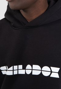 Black hoodie featuring a bold, white graphic text print that reads "SMILODOX," with a relaxed neckline and soft fabric texture.