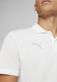 Witte poloshirt van textiel met structuur, voorzien van een kraag met drie knopen en een lichtgrijs logo op de linkerborst.