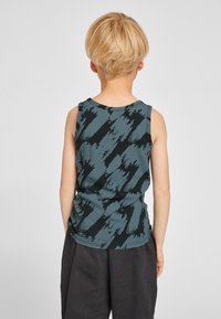 Mouwloze tanktop in teal met zwart penseelstreekpatroon, gemaakt van zachte stof. Ronde halslijn en losse pasvorm. Draagt bij donkere korte broek.