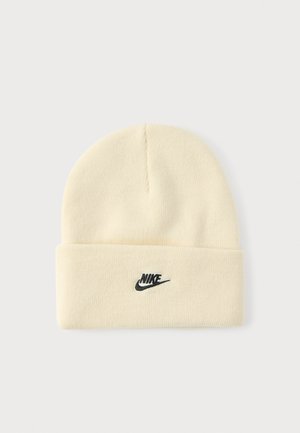 Kremowa dzianinowa czapka z podwiniętym mankietem, z czarnym logo Nike z przodu. Miękka faktura i prosty, zaokrąglony kształt góry.
